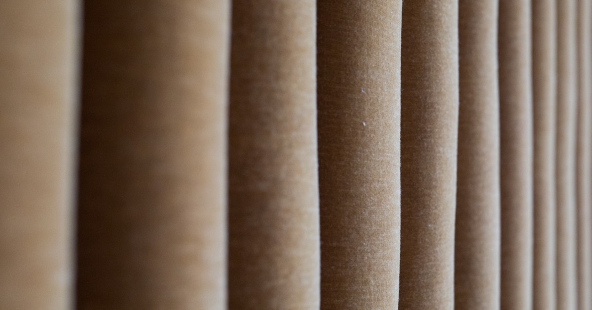 Brown velvet event drapes folded together to create a flowing appearance. Bright light shines on the fabric.